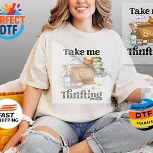 May include: A cream-coloured t-shirt featuring the words "Take me Thrifting" and a graphic of a bread box, bowls, and jars. The shirt is worn by a person.