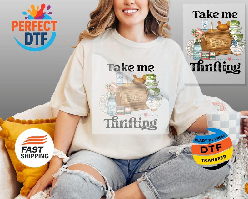 May include: A cream-coloured t-shirt featuring the words "Take me Thrifting" and a graphic of a bread box, bowls, and jars. The shirt is worn by a person.