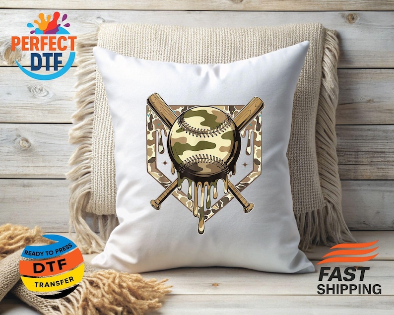 May include: White baseball-themed cushion featuring a camouflage baseball design, two crossed bats, and a home plate outline. The baseball has a dripping effect. The cushion is on a neutral-toned throw.