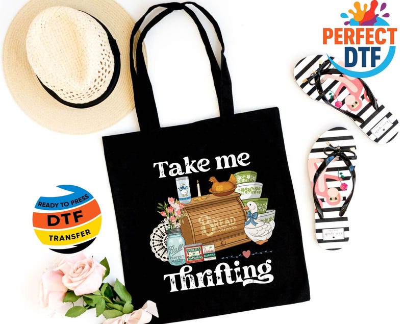 May include: Black tote bag with the text "Take me thrifting" and a graphic of a bread box, bowls, and a duck. A straw hat and black and white striped flip-flops with a flamingo design are also visible.