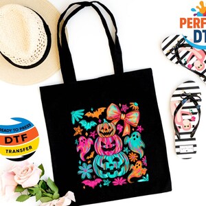 May include: A black tote bag with a colorful Halloween design featuring stacked pumpkins, ghosts, and bats. The image also includes a straw hat and two pairs of black and white striped flip-flops with flamingo designs.