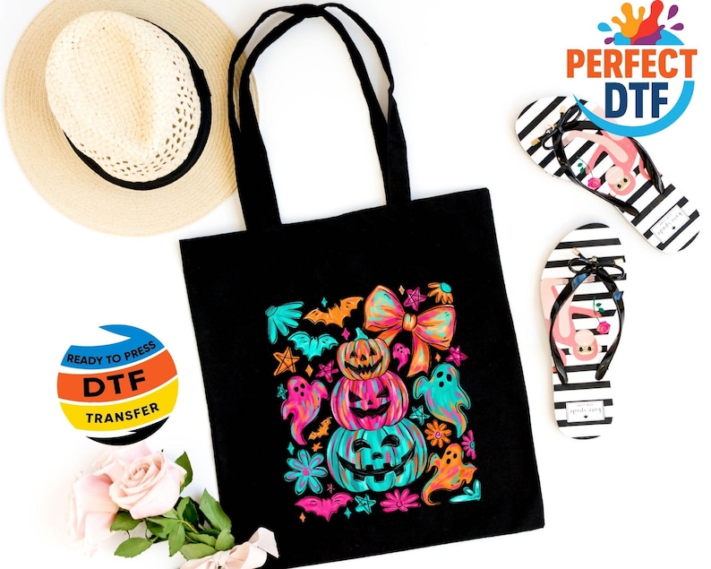 May include: A black tote bag with a colorful Halloween design featuring stacked pumpkins, ghosts, and bats. The image also includes a straw hat and two pairs of black and white striped flip-flops with flamingo designs.