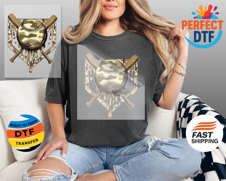 May include: A dark grey t-shirt with a baseball design. The design features a baseball with a camouflage pattern, crossed bats, and a dripping effect. The words "READY TO PRESS DTF TRANSFER" are also visible.