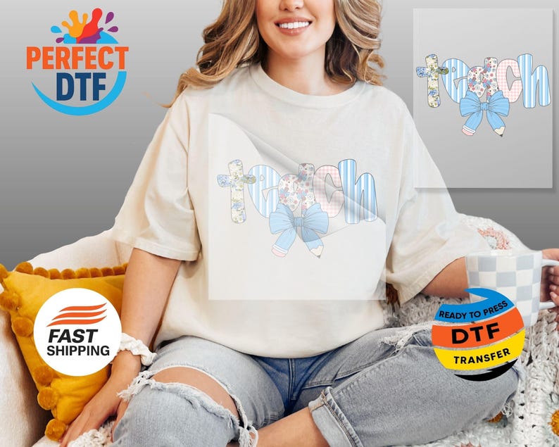 May include: Cream-colored t-shirt with the word "teach" in a whimsical design. The letters feature floral, striped, and bow accents, with pencil details. A light blue bow and pencil graphic is also present.