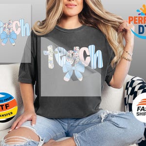 May include: A dark gray t-shirt featuring the word "Teach" in a whimsical design. The letters are adorned with floral patterns, blue stripes, and a light blue bow. The design is likely a DTF transfer.