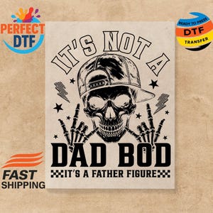 May include: Black and white graphic featuring a skull wearing a backward baseball cap, with the text "IT'S NOT A DAD BOD IT'S A FATHER FIGURE." The design includes stars, lightning bolts, and the skull's hands making a rock-and-roll gesture.