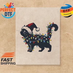 Puede incluir: Un gato negro con un gorro de Papá Noel y envuelto en luces navideñas de colores. El gato está sobre un fondo beige claro. La imagen tiene el texto "PERFECT DTF" y "READY TO PRESS DTF TRANSFER".