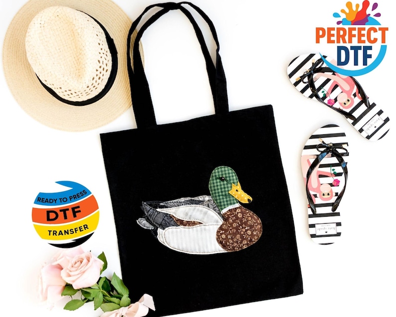 May include: Black tote bag with a duck applique. The duck features green plaid, brown floral, and white fabric. Striped flip-flops with flamingo graphics and a straw hat are also visible.