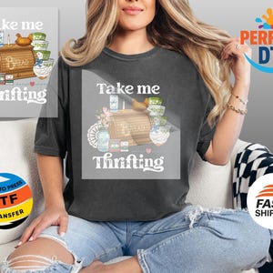 May include: Dark grey t-shirt with the text "Take me Thrifting" and a graphic of a bread box, bowls, flowers, and a duck. The shirt is worn by a person sitting on a white couch.