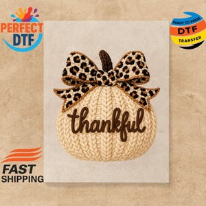 May include: A cream-colored pumpkin design with a leopard print bow and the word "thankful" in brown script. The pumpkin has a knitted texture, perfect for fall-themed crafts and decor.
