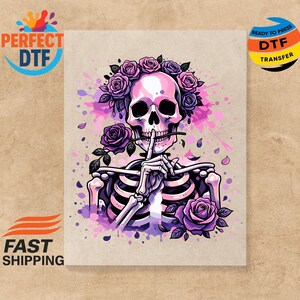 May include: A colorful illustration of a skeleton with a floral crown and roses. The skeleton is holding a finger to its lips in a 'shhh' gesture. The design features shades of pink, purple, and white, with the text "READY TO PRESS DTF TRANSFER".