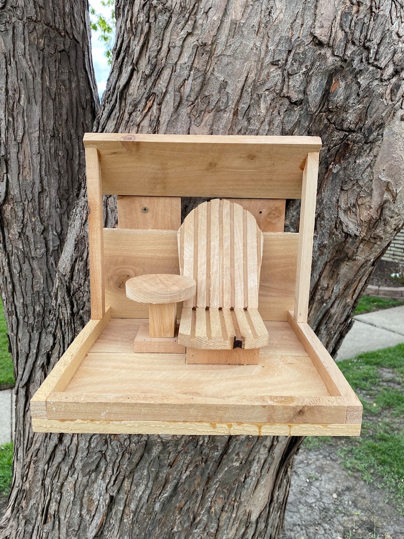 May include: A wooden bird feeder with a small table and a chair, mounted on a tree trunk.