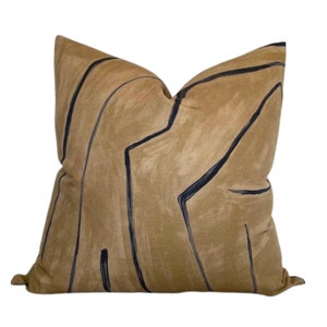 Pode incluir: Uma almofada de lançamento de cor bege com um padrão geométrico em azul escuro. O padrão é composto por linhas e formas.