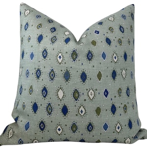May include: A decorative throw pillow with a light green background and a repeating pattern of blue, white, and olive-green diamond shapes. The pillow has a soft, textured appearance and a classic design.