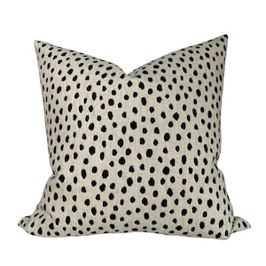 Puede incluir: Una almohada beige con un patrón de lunares negros.
