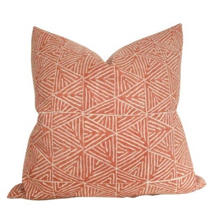 May include: A coral orange throw pillow with a geometric pattern of white lines forming triangles.