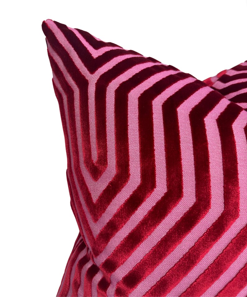 May include: A red and pink chevron patterned throw pillow with a soft velvet texture.