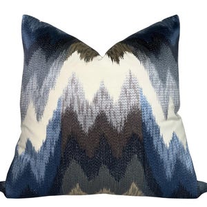 May include: Square cushion featuring a geometric zigzag design in blue, grey, and brown hues. The cushion has a cream backdrop and a textured finish, ideal for home decoration. Measures approximately 40cm x 40cm.