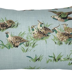 Peut inclure: Coussin rectangulaire avec un fond bleu clair orné d'un motif répété d'oiseaux dans un champ herbeux. Les oiseaux sont représentés dans des tons de marron, de vert et de blanc. De l'herbe verte et du feuillage sont également présents.