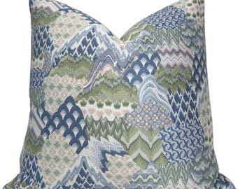 Pode incluir: Uma almofada quadrada com um design têxtil complexo e variado. O tecido apresenta um mosaico de formas geométricas, incluindo ziguezagues, escamas e motivos florais numa paleta de cores verde sálvia, azul marinho e branco suave.