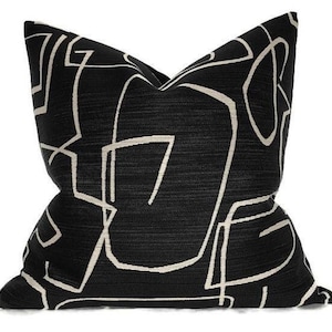 May include: A black cushion with a cream-coloured abstract geometric design. The cushion has a textured appearance and a square shape, suitable for a sofa or bed. The design features interconnected lines.