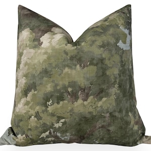 May include: Square decorative pillow with a watercolor-style forest scene in shades of green, brown, and white. The pillow has a soft, textured appearance, suggesting a linen or similar fabric. The design evokes a natural, outdoorsy aesthetic.