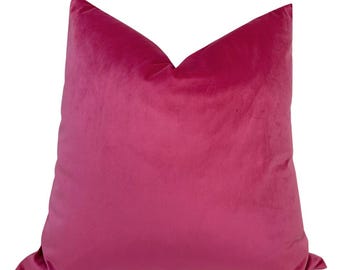 May include: A square throw pillow cover in a solid, vibrant magenta pink color. The fabric has a soft, short-pile velvet texture that catches the light, creating subtle variations in tone across the surface of the square-shaped cushion.