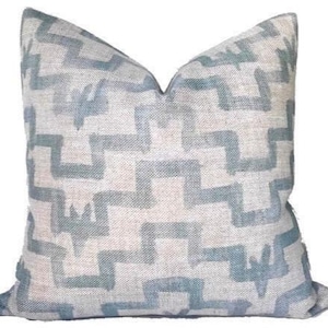 May include: Square decorative pillow with a geometric pattern in shades of blue and beige. The pillow features a textured fabric and a zig-zag design, adding a touch of modern style to any room. The pillow measures approximately 18 inches square.