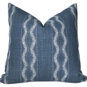 May include: A square throw cushion featuring a deep blue fabric base with a visible woven texture. The surface is decorated with vertical, repeating white wavy line patterns that run parallel across the front of the cushion cover.