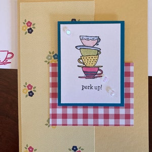 May include: A yellow card with a red and white checkered pattern and a teal blue frame with a stack of colorful teacups and the text "perk up!"