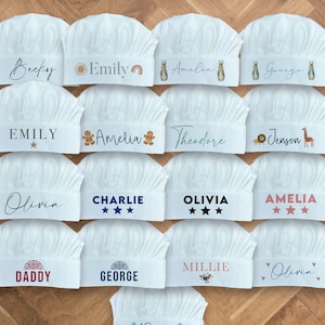 Könnte beinhalten: Eine Sammlung von 15 weißen Kochmützen mit verschiedenen Namen und Designs, die darauf gedruckt sind. Die Namen sind Becky, Emily, Amelia, George, Jenson, Theodore, Olivia, Charlie, Millie, Reuben und Daddy. Einige Mützen haben Sterne, Herzen und andere dekorative Elemente.