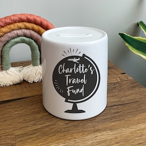 Puede incluir: Huchita de cerámica blanca con un diseño de globo negro y el texto "Charlotte's Travel Fund".