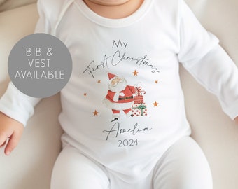 May include: White baby onesie with a red and white Santa Claus illustration, gold stars, and the text "My First Christmas Amelia 2024".