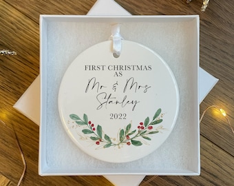 Può includere: Addobbo natalizio in ceramica bianca con foglie di agrifoglio verdi e bacche rosse. L'addobbo recita "First Christmas as Mr. & Mrs. Stanley 2022".