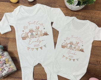 May include: Two white baby onesies with long and short sleeves. The onesies feature a graphic of bunnies and the text "My First Easter" with a name and the year 2023.