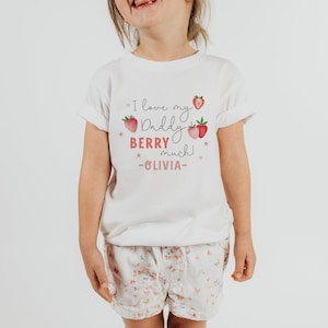 May include: White t-shirt with a pink and red strawberry graphic and the text "I love my Daddy Berry much! -OLIVIA-"