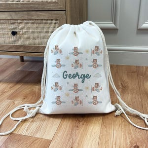 May include: A white canvas drawstring bag with a personalized name "George" printed on it. The bag features a repeating pattern of cute cartoon bears flying airplanes with green, blue, and yellow accents.