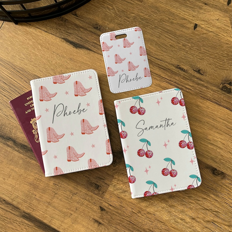 May include: Three passport holders with different designs. One has a pink cowboy boot pattern with the name "Phoebe" on it. Another has a red cherry pattern with the name "Samantha" on it. The third has a pink cowboy boot pattern with the name "Phoebe" on it.