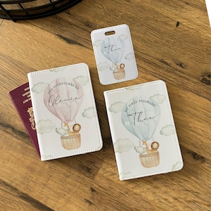 May include: A collection of personalized travel accessories, including a passport holder, luggage tag, and passport cover. Each item features a hot air balloon design with the name "Theo" or "Olivia" and the phrase "My First Passport" or "The Adventures of".