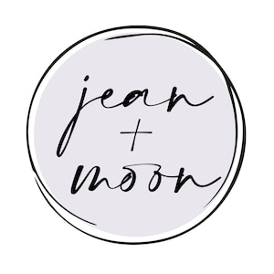 May include: A logo with the text "jean + moon" in a handwritten, cursive style. The black text is set within a light purple circle, which is surrounded by a black, hand-drawn outline. The background is white.