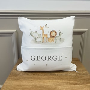 May include: White pillow with a pocket on the front. The pillow has a print of a giraffe, elephant, lion, and zebra with a crown on the elephant and lion. The text "GEORGE" is printed on the pocket.