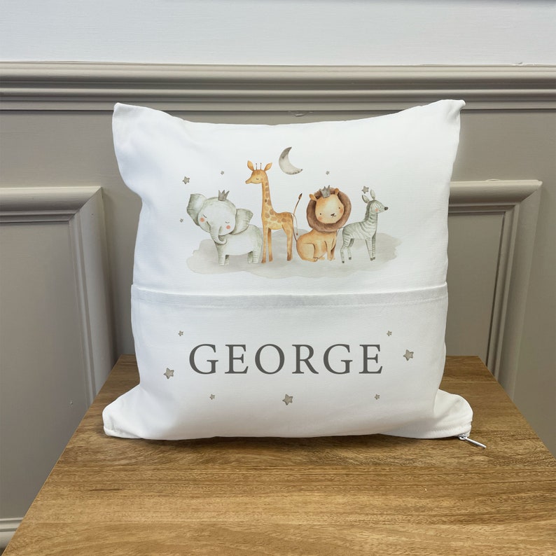 May include: White pillow with a pocket on the front. The pillow has a print of a giraffe, elephant, lion, and zebra with a crown on the elephant and lion. The text "GEORGE" is printed on the pocket.