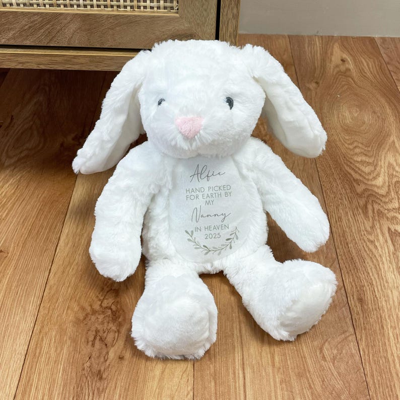 May include: White plush bunny rabbit with long ears. The bunny has a pink nose and is embroidered with the text "Alfie Hand Picked For Earth By My Nanny In Heaven 2023".