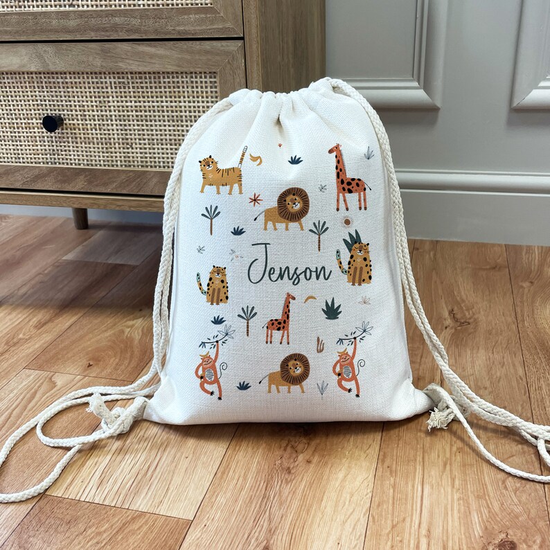 May include: A white drawstring bag with a jungle animal print. The bag features lions, tigers, giraffes, and monkeys. The name "Jenson" is printed on the bag.