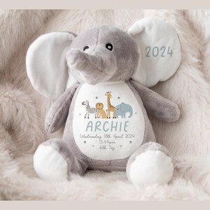 May include: A gray plush elephant stuffed animal with a white patch on its chest. The patch features a zebra, lion, giraffe, and elephant illustration, along with the name "Archie", the date "Wednesday 18th April 2024", the time "15:44pm", and the text "6lb 7oz". The elephant's ear has the year "2024" embroidered on it.