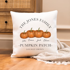 Op de afbeelding: Een wit kussen met de tekst "The Jones Family - Pumpkin Patch - Locally Grown" en vier oranje pompoenen met de namen Lola, Emma, Jack en Ethan eronder.