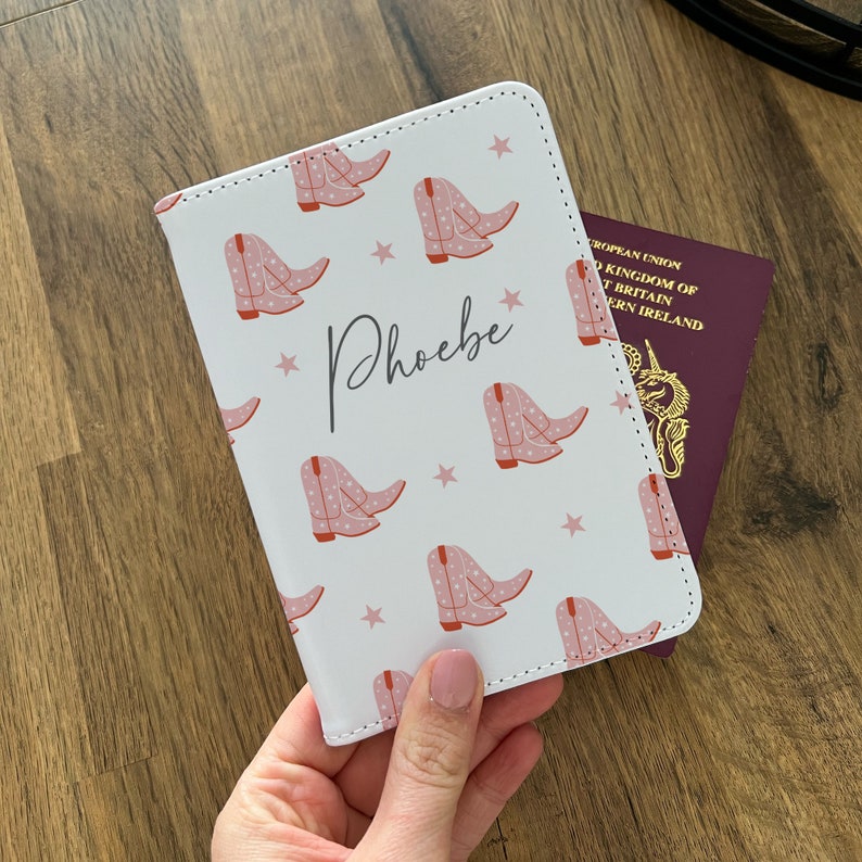 May include: White passport holder with a pink and white cowboy boot pattern and the name "Phoebe" written in cursive.