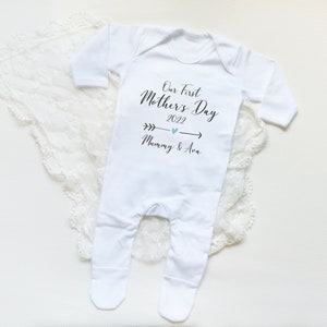May include: White baby onesie with black text that reads "Our First Mother's Day 2022 Mummy & Ava" with a blue arrow and heart.