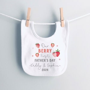 May include: White baby bib with red strawberries and the text "Our Berry First Father's Day -Daddy & Sophia- 2024".