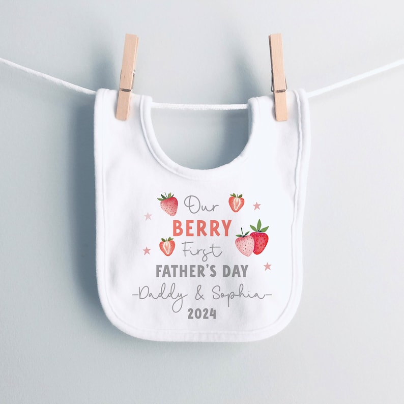 May include: White baby bib with red strawberries and the text "Our Berry First Father's Day -Daddy & Sophia- 2024".